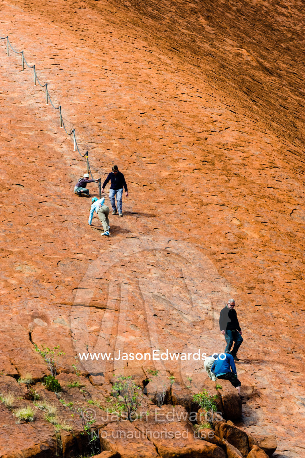 Uluru dwarfs tourists and walkers using a chain to climb its steep, smooth, oxidized slopes. Uluru Kata Tjuta National Park, Northern Territory, Australia.
