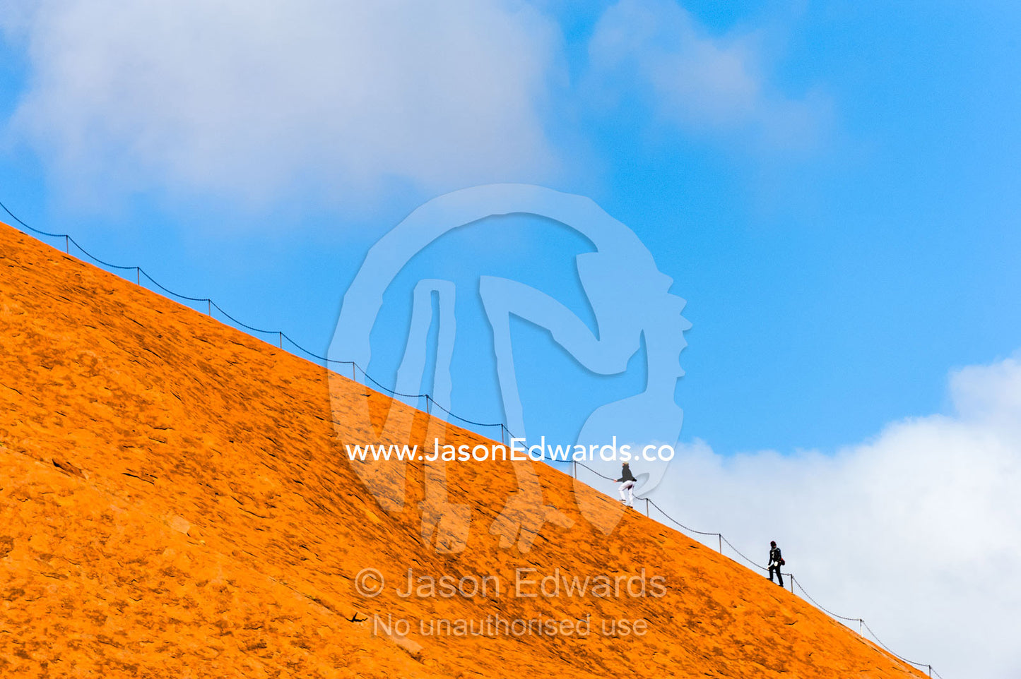 Uluru dwarfs tourists and walkers using a chain to climb its steep, smooth, oxidized slopes. Uluru Kata Tjuta National Park, Northern Territory, Australia.