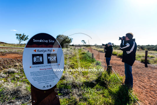 Tourists photograph an area of Uluru near an Aboriginal sacred site despite a sign forbidding it. Uluru Kata Tjuta National Park, Northern Territory, Australia.