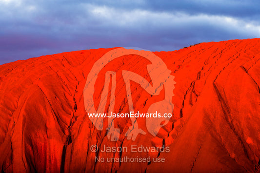 Sunlight casts shadows in the folds and fissures of the blood red sandstone of Uluru at sunset. Uluru Kata Tjuta National Park, Northern Territory, Australia.