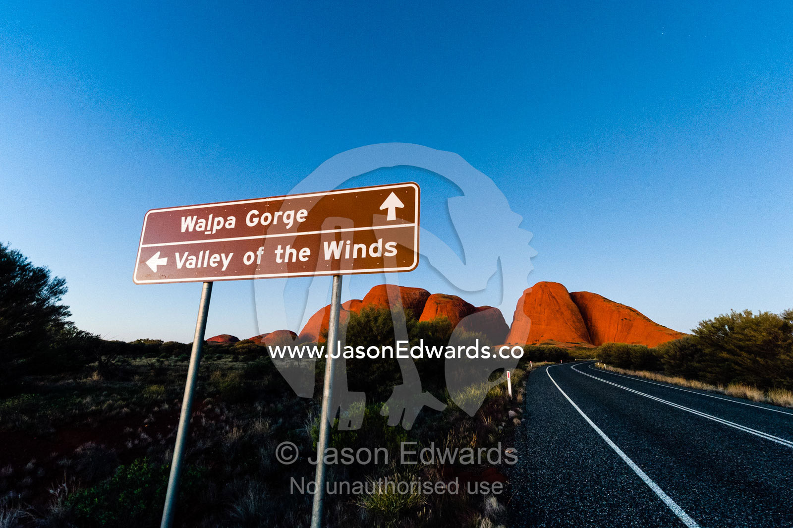 A road and directional sign on the outback desert plain near the domes of Kata Tjuta at sunset. Uluru Kata Tjuta National Park, Northern Territory, Australia.
