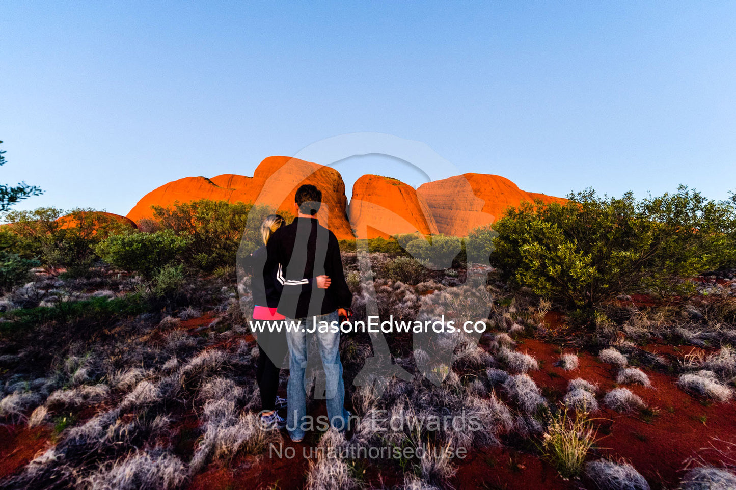 A couple enjoys a desert sunset as it illuminates the domes of Kata Tjuta. Uluru Kata Tjuta National Park, Northern Territory, Australia.