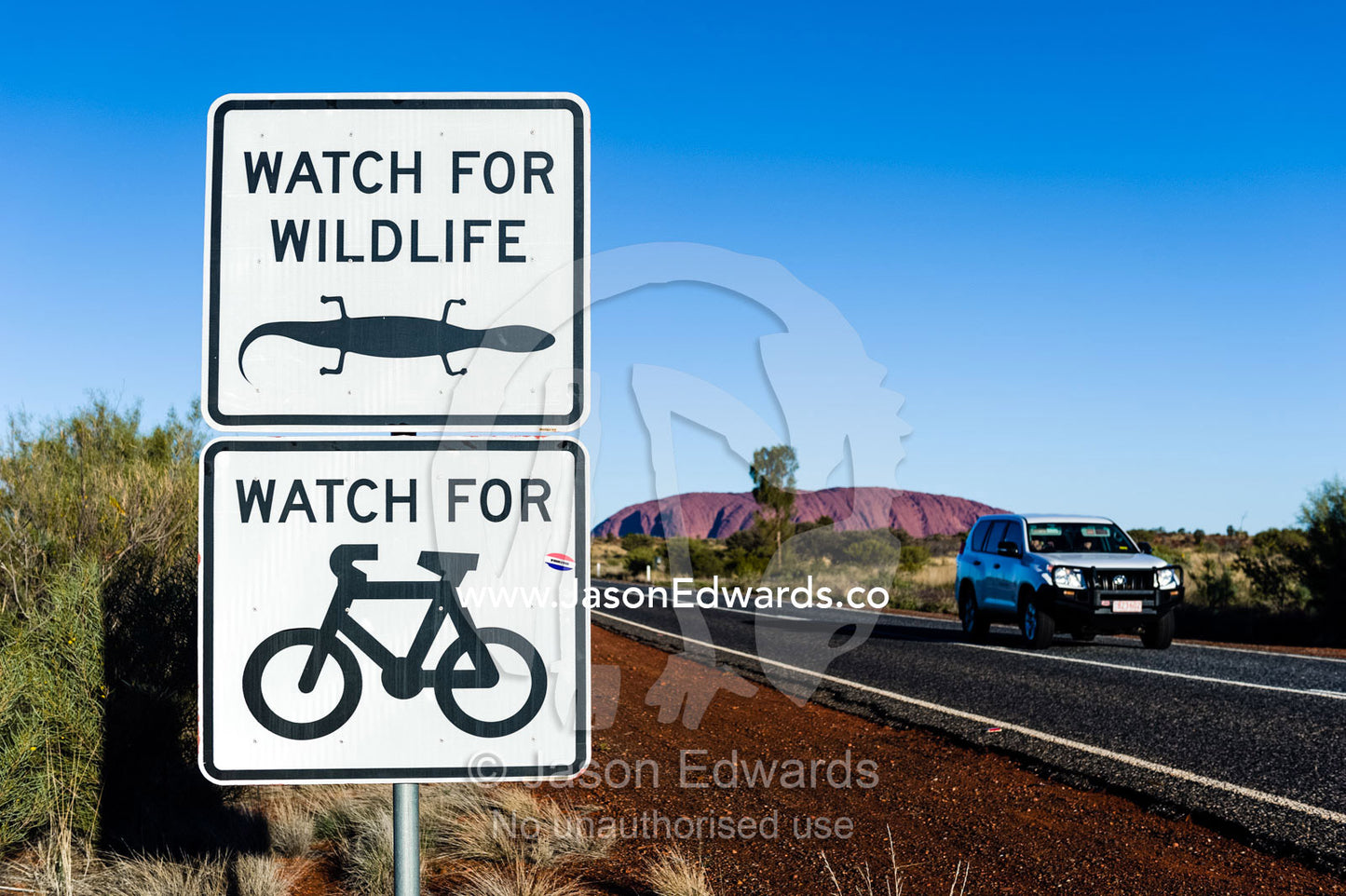 A 4wd passes a sign warning cyclists and vehicle drivers to beware of wildlife on the road near Uluru. Uluru Kata Tjuta National Park, Northern Territory, Australia.