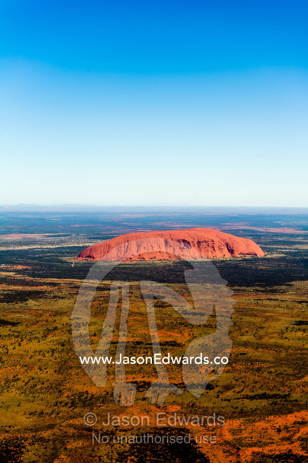The ochre sandstone dome of Uluru rises from a vast desert plain in Australia's Outback. Uluru Kata Tjuta National Park, Northern Territory, Australia.