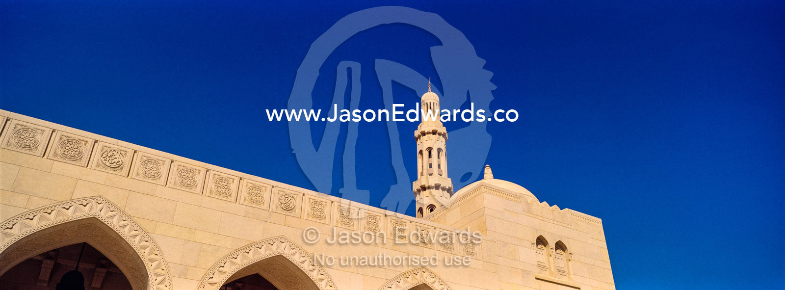 An ornate stone minarette rises above a carved white sandstone wall in the Grand Mosque. Sultan Qaboos Grand Mosque, Muscat, Sultanate of Oman.