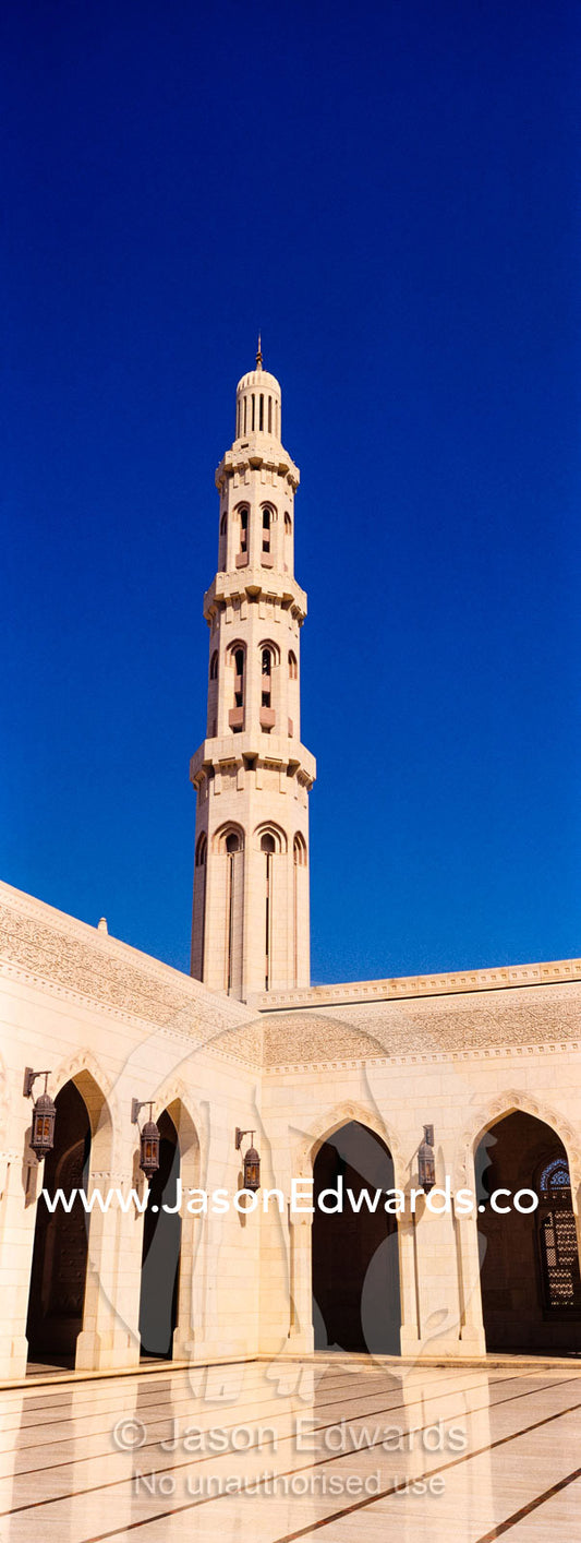 An ornate stone minarette towers over a polished paved courtyard in the Grand Mosque. Sultan Qaboos Grand Mosque, Muscat, Sultanate of Oman.