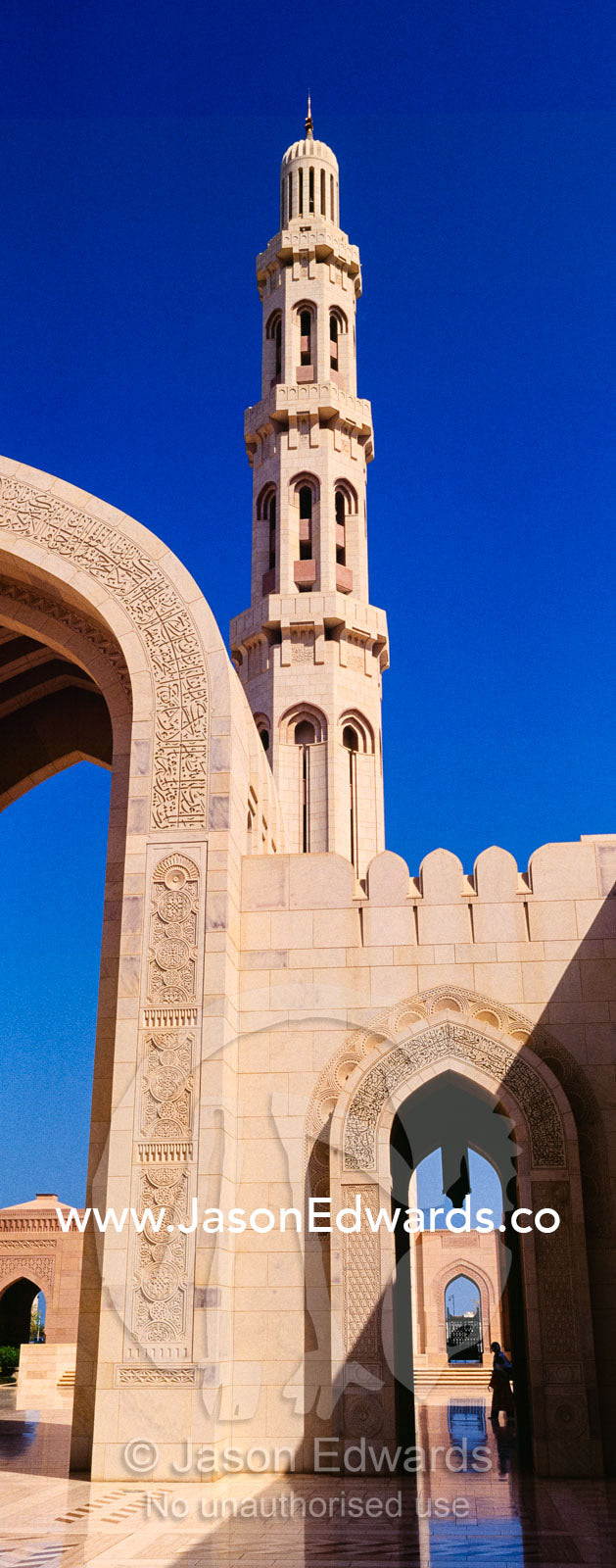 An ornate stone minarette towers over a polished paved courtyard in the Grand Mosque. Sultan Qaboos Grand Mosque, Muscat, Sultanate of Oman.