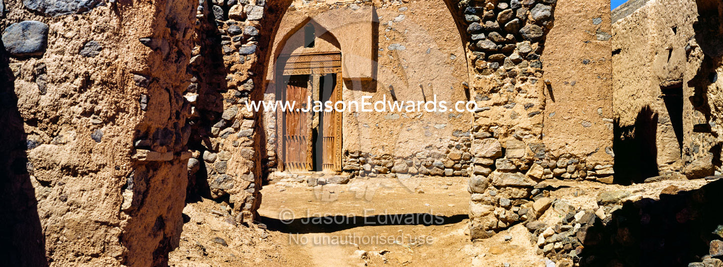 Crumbling walls and market archways collapse back into the desert in an ancient abandoned village. Ibra, Ash Sharqiyah Region, Sultanate of Oman.