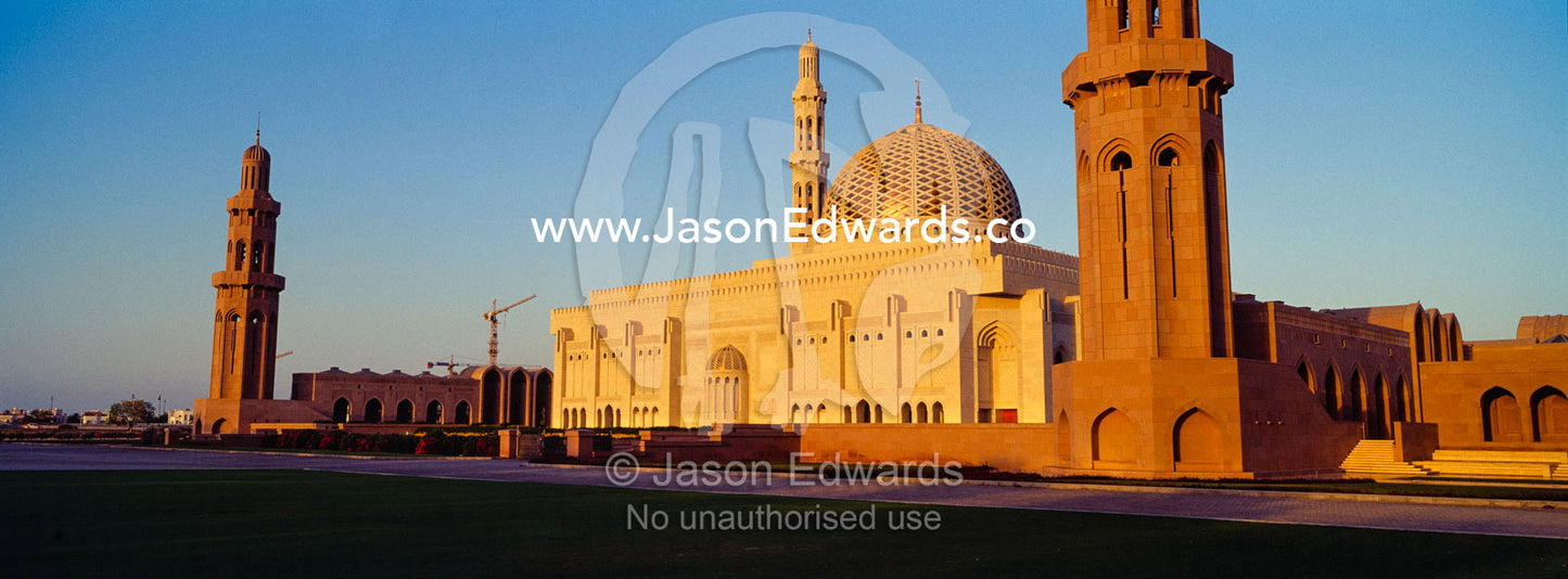 An ornate stone minaret towers over the dome of the Prayer Hall of the Grand Mosque at sunset. Sultan Qaboos Grand Mosque, Muscat, Sultanate of Oman.