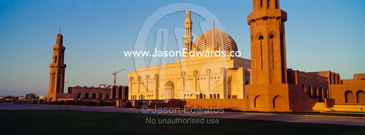 An ornate stone minaret towers over the dome of the Prayer Hall of the Grand Mosque at sunset. Sultan Qaboos Grand Mosque, Muscat, Sultanate of Oman.