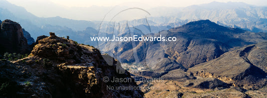 The steep slopes of arid jagged mountains overlooking an eroded and inhospitable rocky desert valley. Jebel Shams, Al Hajar Mountains, Sultanate of Oman.