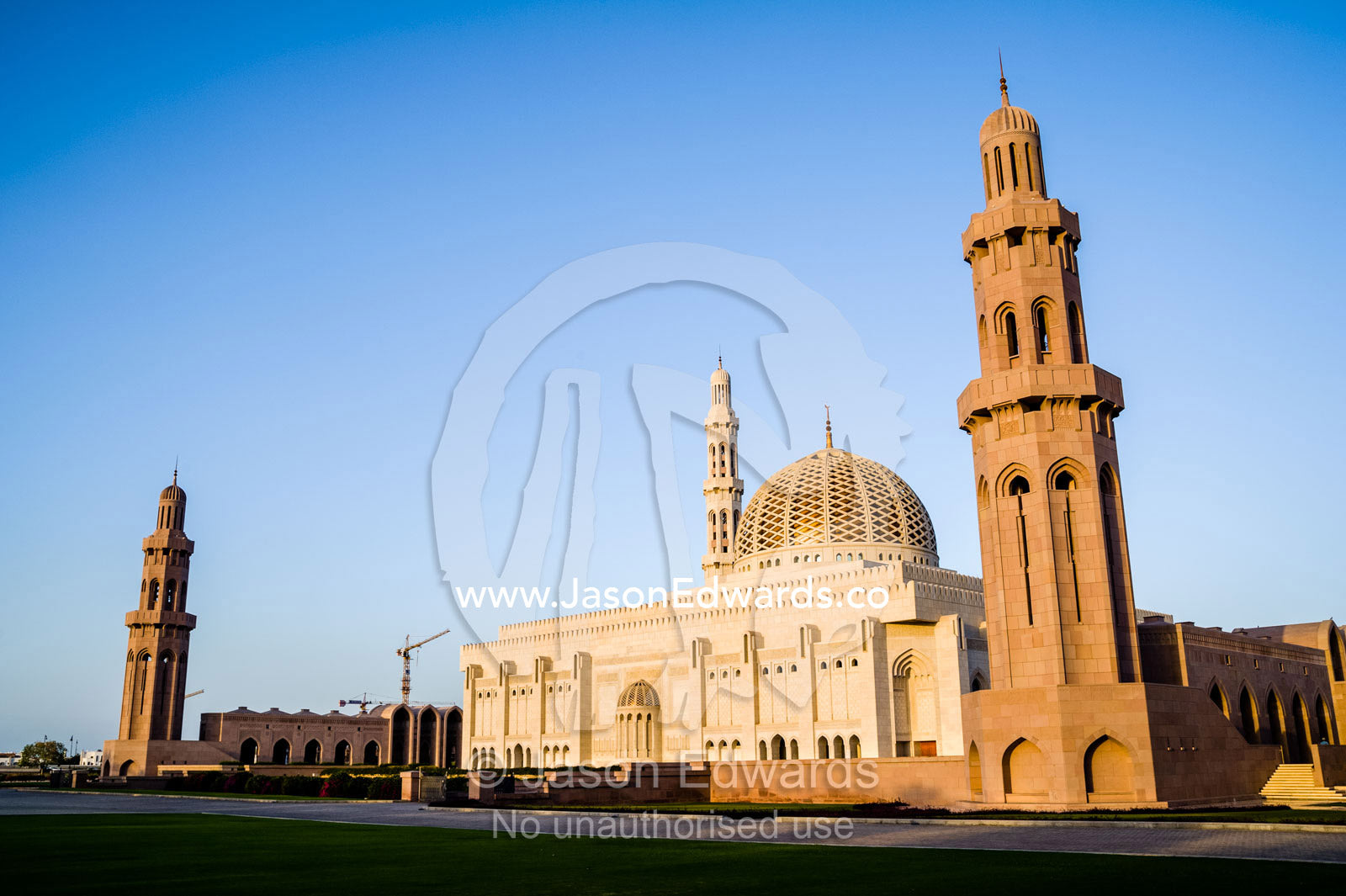 An ornate stone minarette towers over the dome of the Prayer Hall of the Grand Mosque at sunset. Sultan Qaboos Grand Mosque, Muscat, Sultanate of Oman.