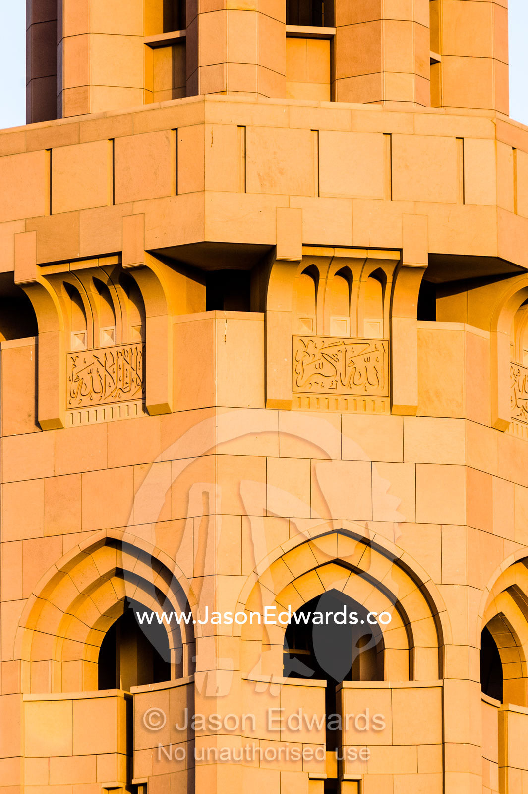 A balcony on an ornate stone minaret that towers over the dome of the Prayer Hall of the Grand Mosque at sunset. Sultan Qaboos Grand Mosque, Muscat, Sultanate of Oman.
