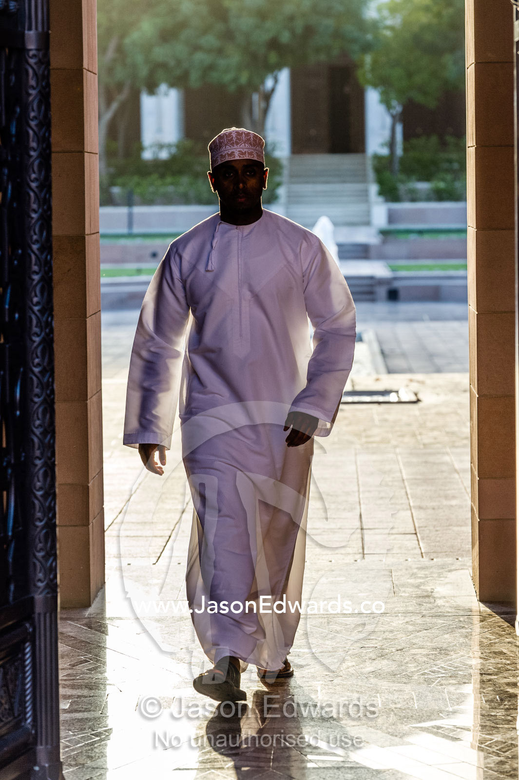 A Muslim man wearing a traditional kuma and dishdasha walking through the Grand Mosque. Sultan Qaboos Grand Mosque, Muscat, Sultanate of Oman.