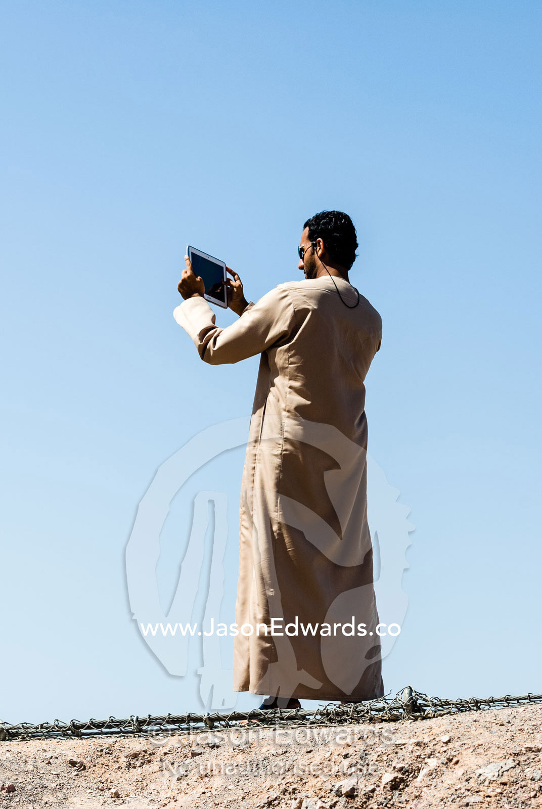 A man from Oman wearing a dishdasha taking photographs with a tablet device. Muscat, Sultanate of Oman.