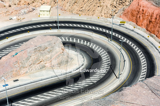 A curved road covered in stripes winding it's way up a mountainside. Muscat, Sultanate of Oman.