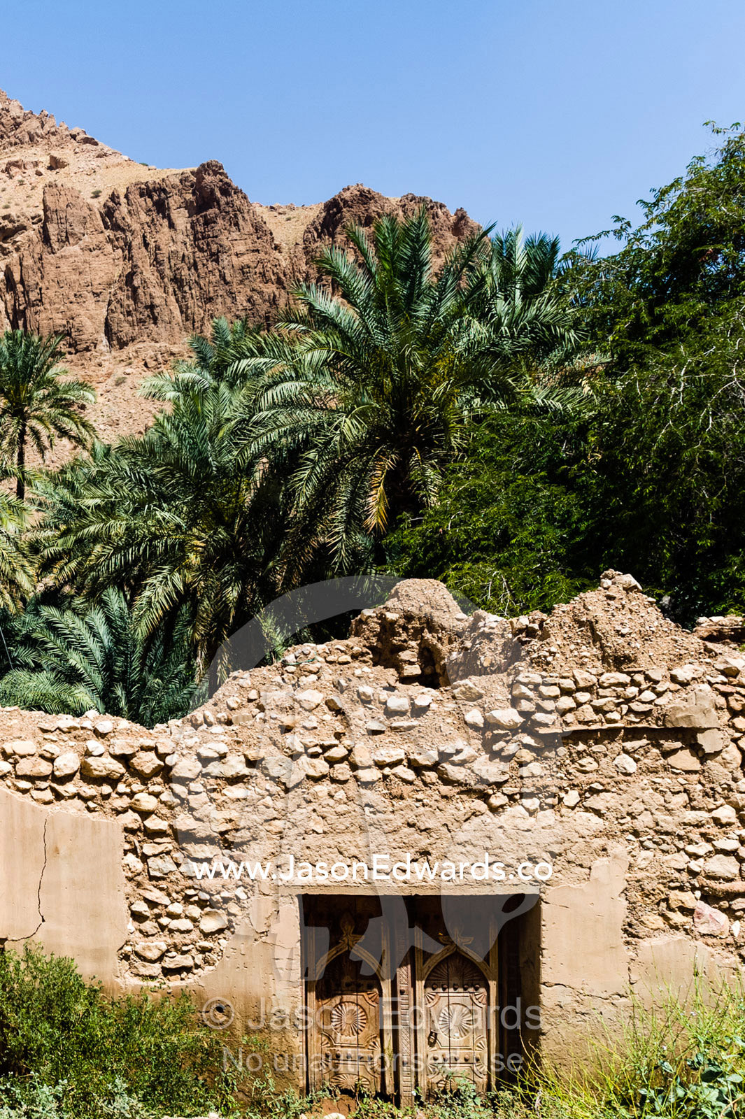 An ancient mud and stone wall with timber doors surrounding a palm plantation. Mibam, Wadi Tiwi, Sur Al Sharqiyah South Governorate, Sultanate of Oman.