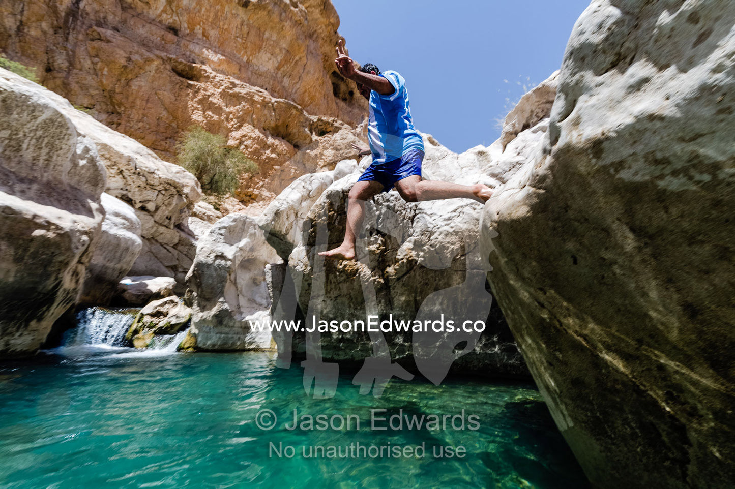 A tourist leaps into the turquoise waters of a wadi in a desert valley to cool off. Wadi Bani Khalid, Sharqiyah Region, Sultanate of Oman.