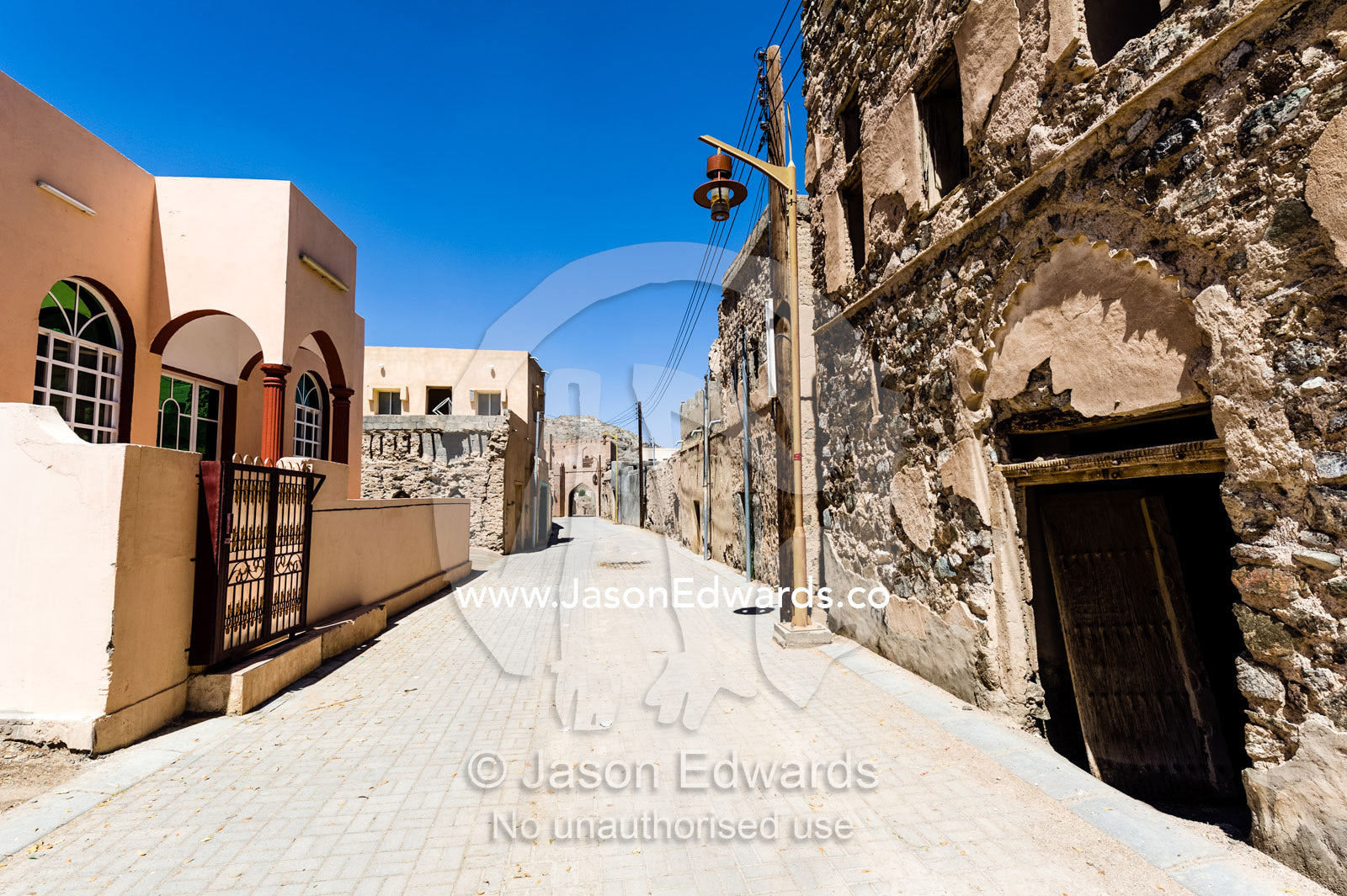 New homes and ancient dwellings line a narrow street in an abandoned village in the desert. Ibra, Ash Sharqiyah Region, Sultanate of Oman.