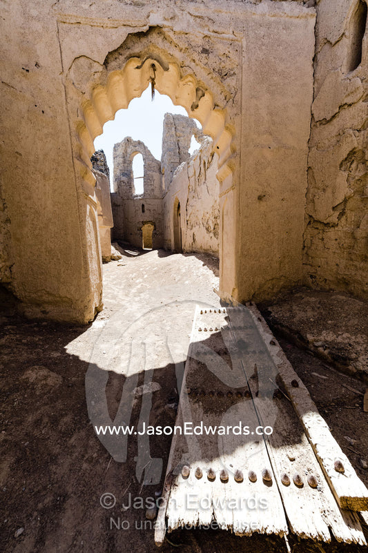 Ornate scalloped stone and mudbrick archways above a fallen timber door in an abandoned village in the desert. Ibra, Ash Sharqiyah Region, Sultanate of Oman.