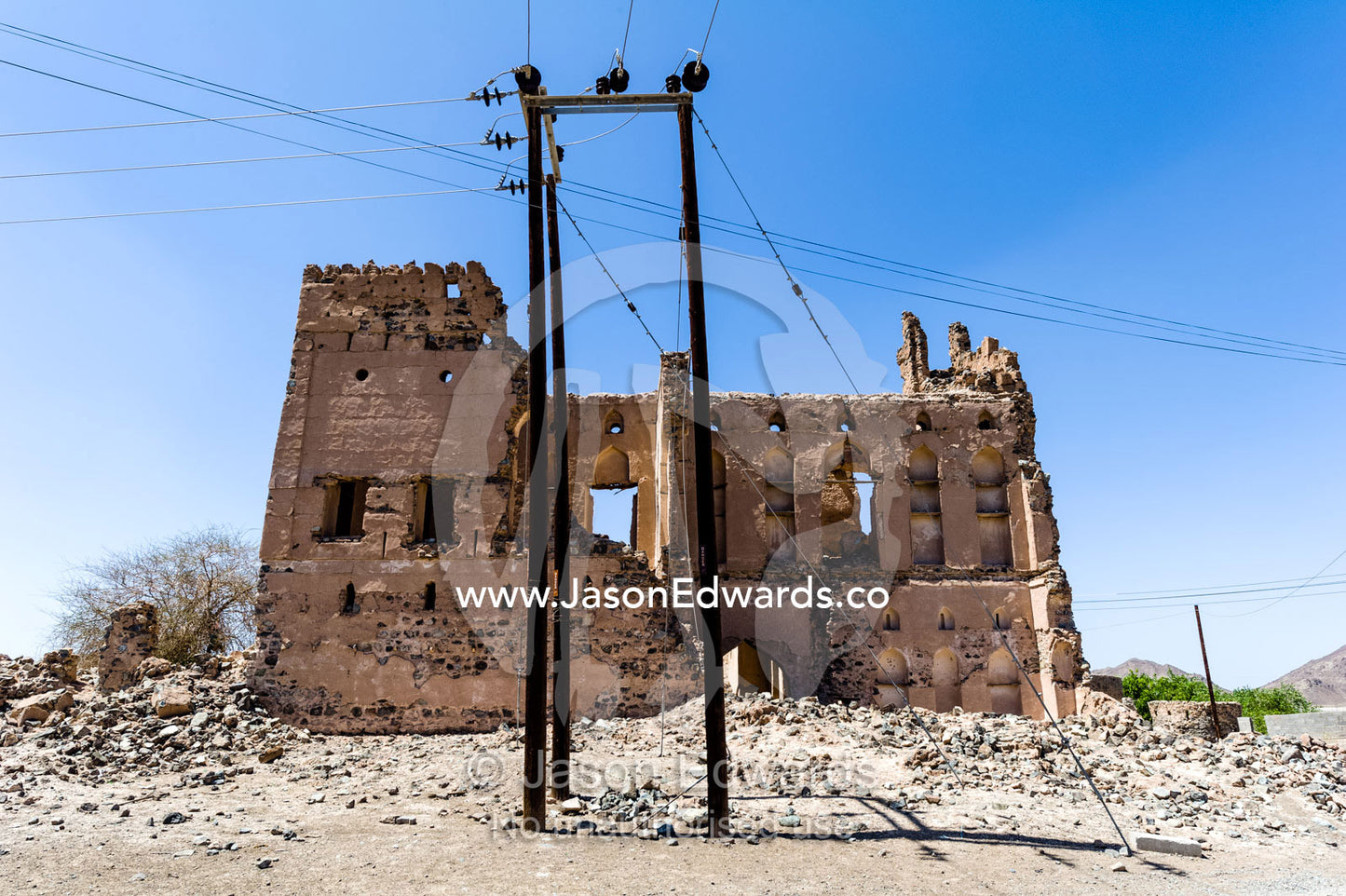 Rusting electricity poles beside an ancient crumbling ruin in a desert village. Ibra, Ash Sharqiyah Region, Sultanate of Oman.