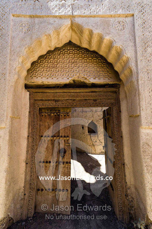 Ornate scalloped stone and mudbrick archways above carved timber lintels and doorways in an abandoned village in the desert. Ibra, Ash Sharqiyah Region, Sultanate of Oman.