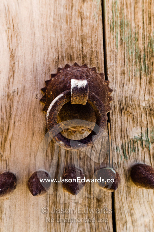A rusting steel knocker on a timber door in an ancient desert village. Ibra, Ash Sharqiyah Region, Sultanate of Oman.