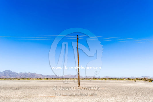 A solitary electricity pole running through a flat and barren desert. Nizwa, Sultanate of Oman.