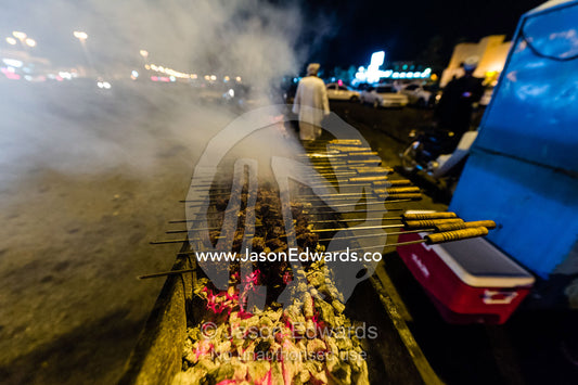 Smoke rises from meat kebabs grilling on hot coals in a night market. Muscat, Sultanate of Oman.