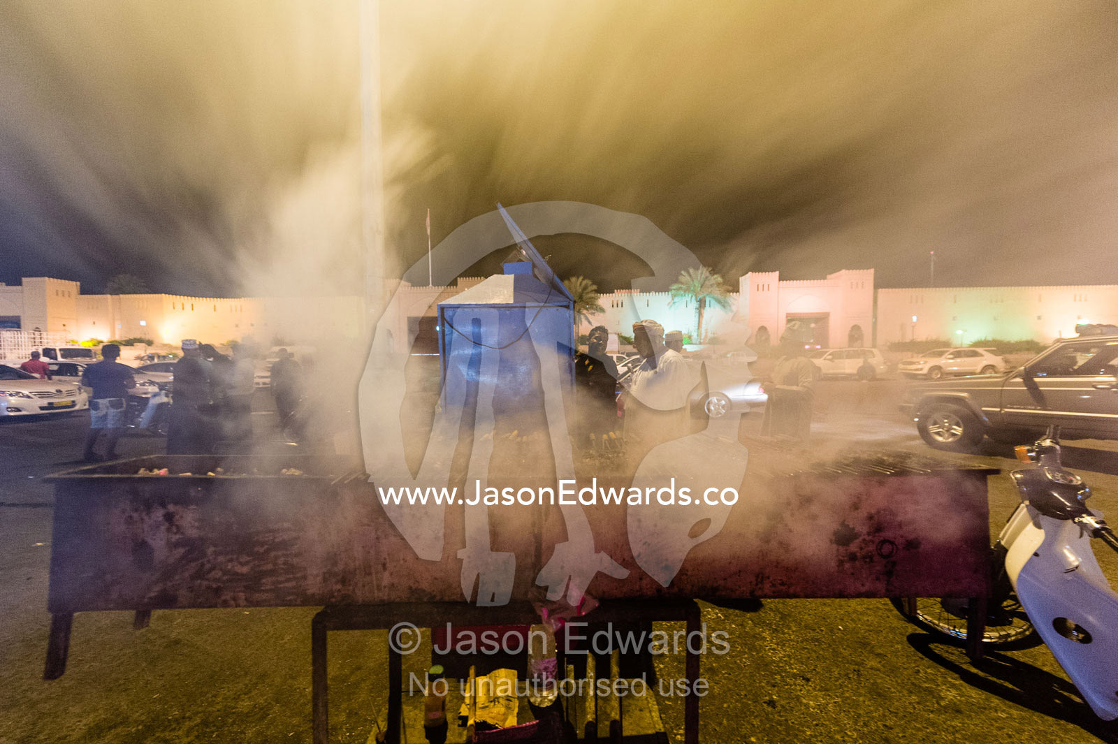 Smoke rises from meat kebabs grilling on hot coals in a night market. Muscat, Sultanate of Oman.