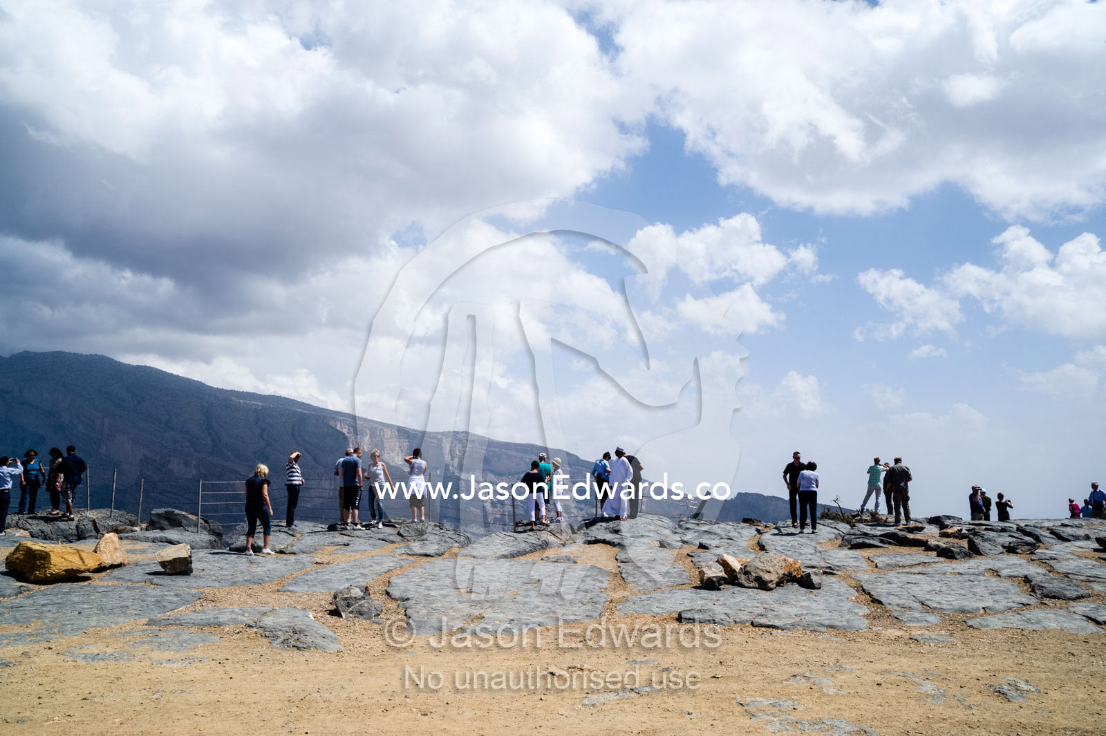 Tourists view the sheer cliff walls and terraces carved by erosion in a massive desert canyon. Wadi Ghul, Jebel Shams, Al Hajar Mountains, Sultanate of Oman.