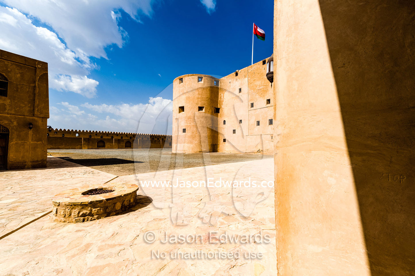 A well in a vast forecourt surrounded by imposing walls and watchtowers in an ancient fort. Jabrin Fort, Ad Dakhiliyah Governorate, Sultanate of Oman.