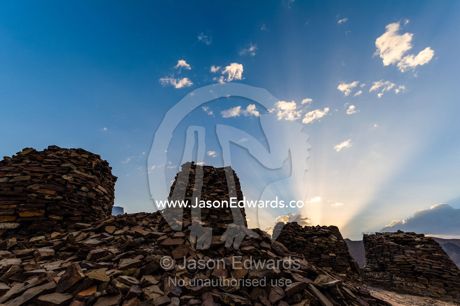Dawn sun rays rise over ancient handmade stone burial mounds and tombs atop a desert ridge. Archaeological Sites of Bat, Al-Ayn, Al Dhahira Region, Sultanate of Oman.