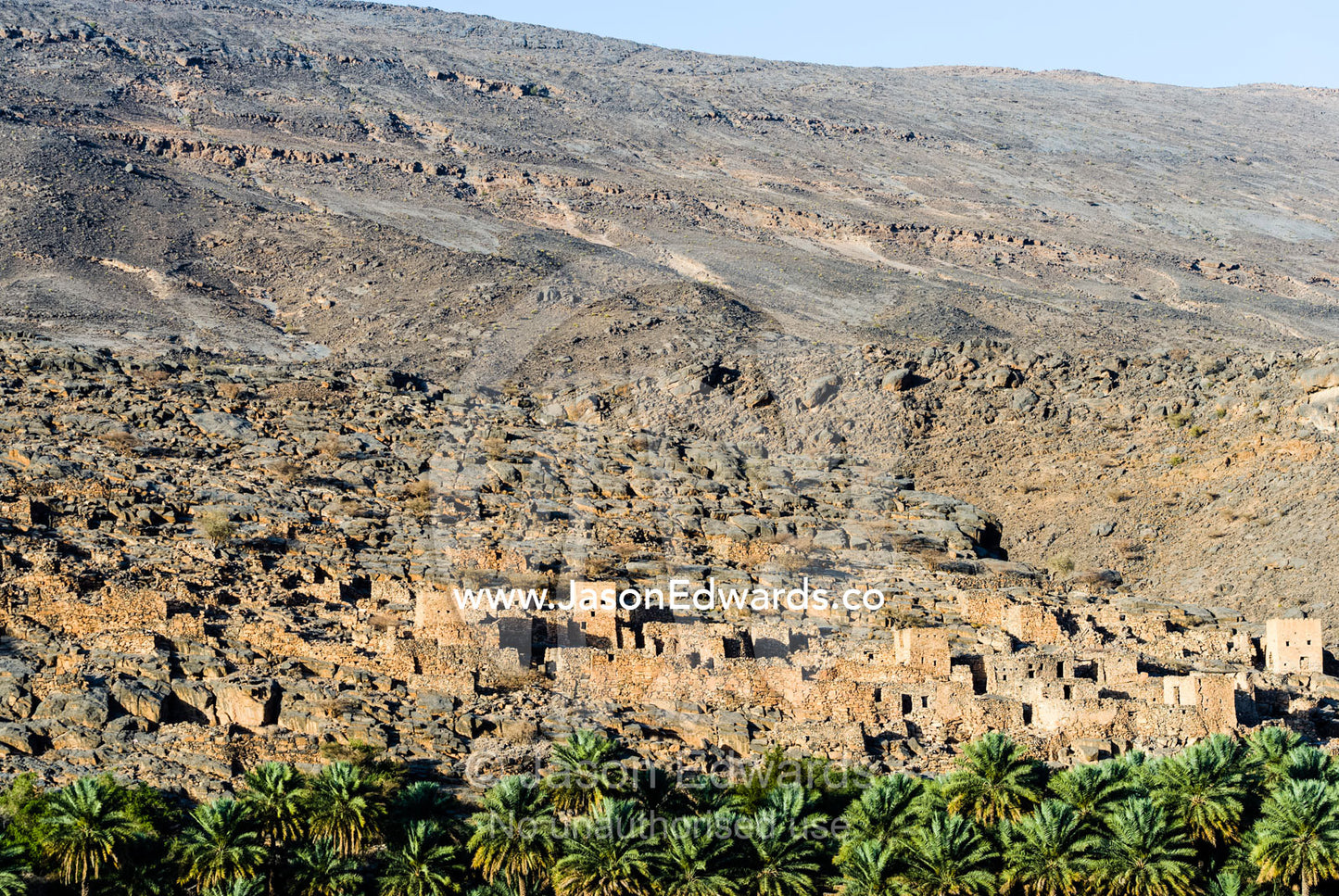An ancient abandoned stone village on a desert mountainside above an irrigated Date Palm plantation. Wadi Nakhar, Al Hamra, Ad Dakhiliyah Region, Sultanate of Oman.