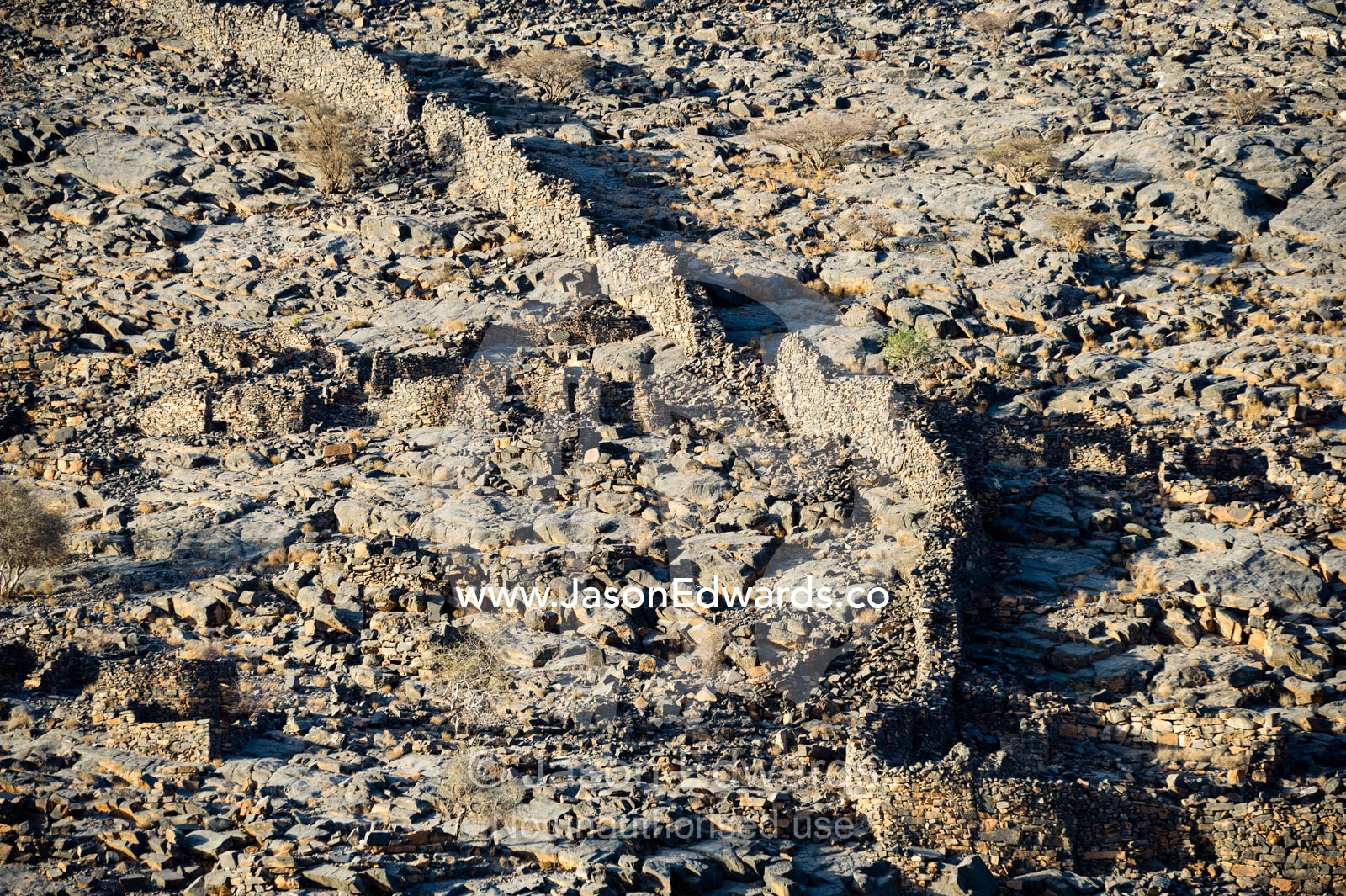 The defensive wall of an ancient abandoned stone village on a desert mountainside. Wadi Nakhar, Al Hamra, Ad Dakhiliyah Region, Sultanate of Oman.