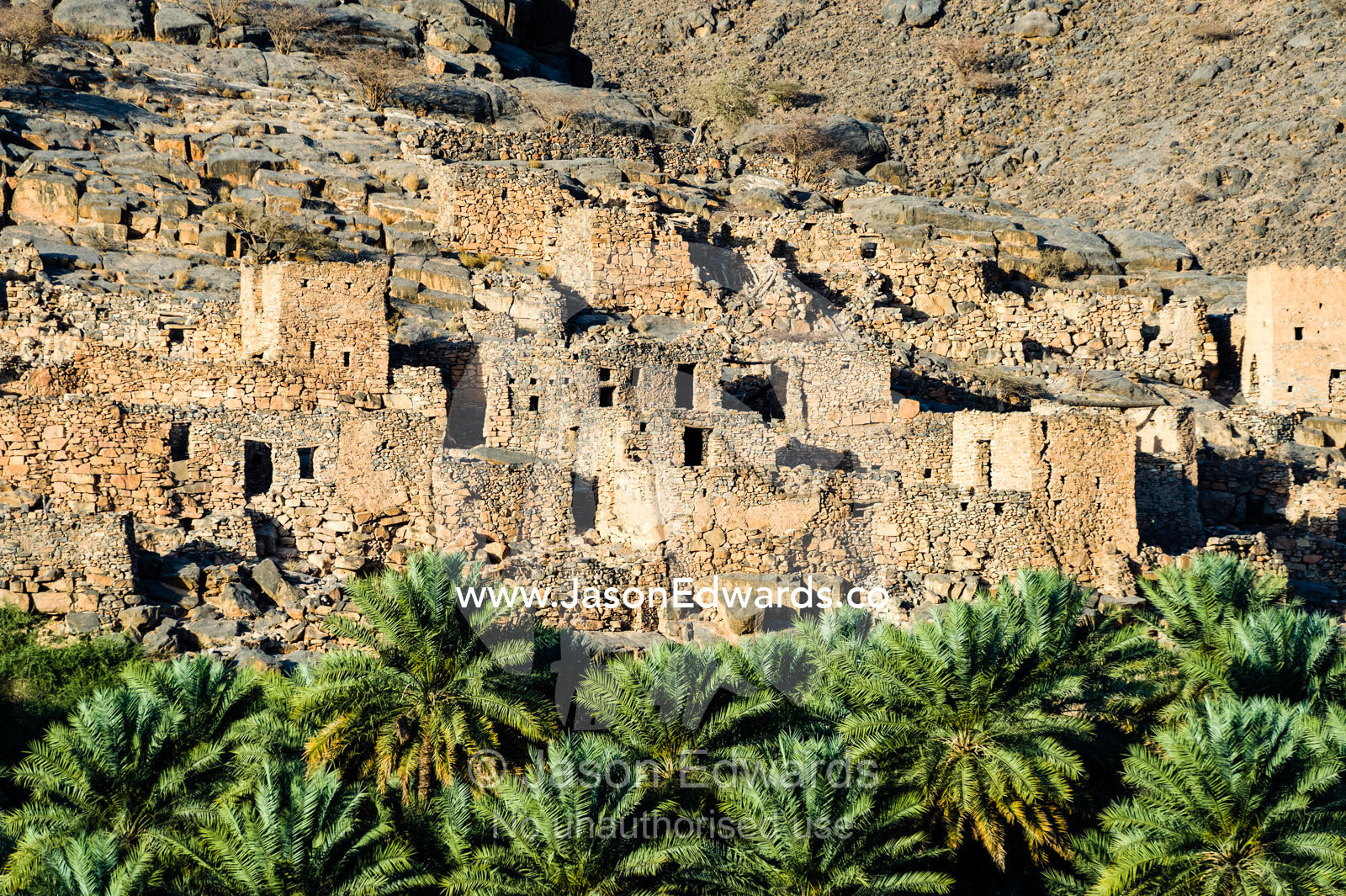 An ancient abandoned stone village on a desert mountainside above an irrigated Date Palm plantation. Wadi Nakhar, Al Hamra, Ad Dakhiliyah Region, Sultanate of Oman.