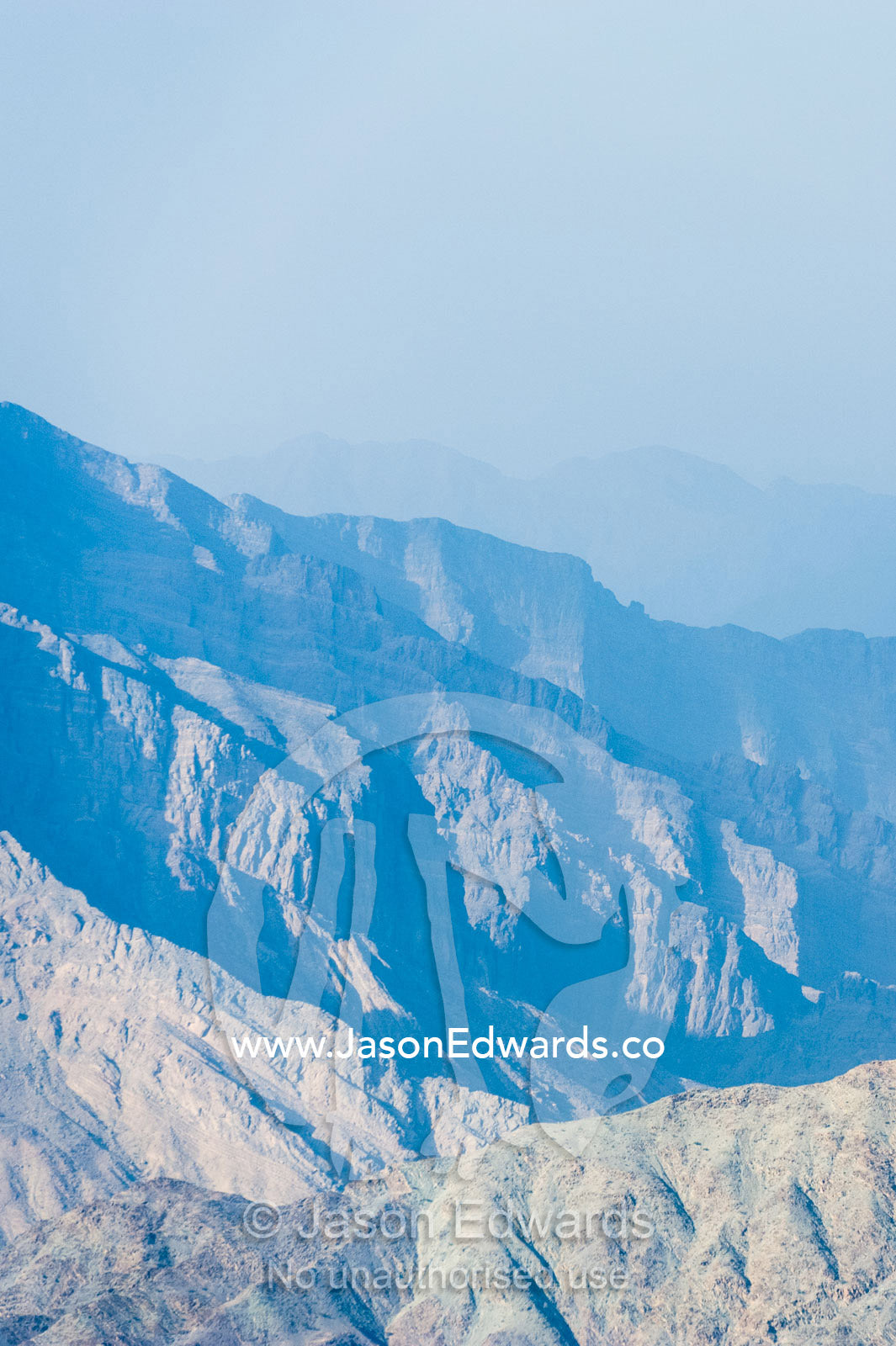 The steep slopes of arid jagged mountains overlooking an eroded and inhospitable rocky desert valley. Hatt, Wadi Bani Awf, Snake Gorge, Western Hajar Mountains, Ad Dakhiliyah Region, Sultanate of Oman.