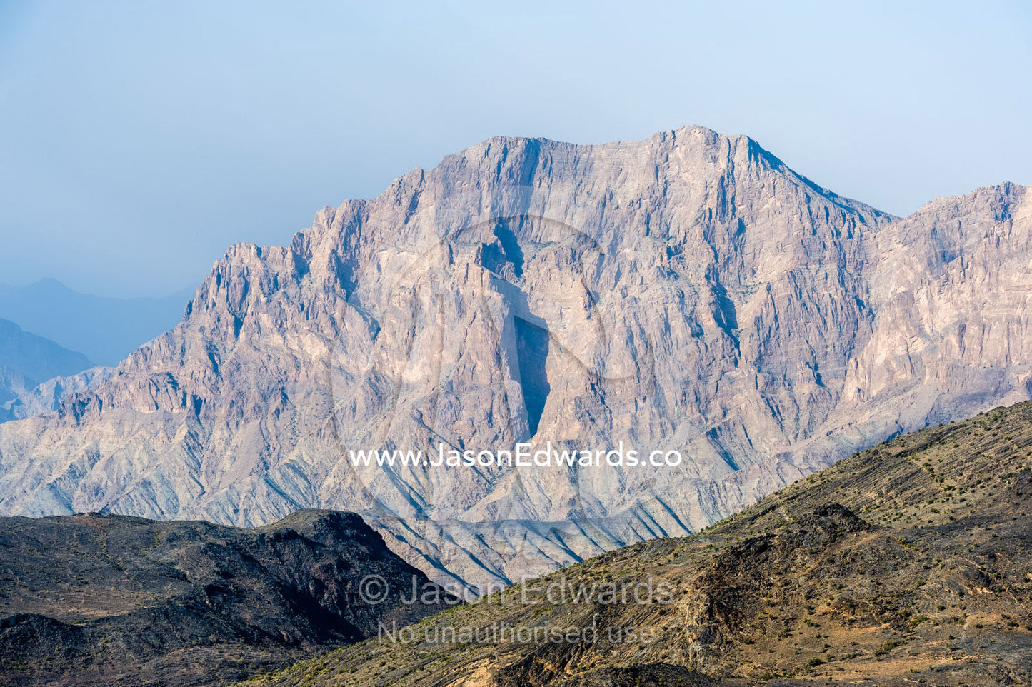 The steep slopes of arid jagged mountains overlooking an eroded and inhospitable rocky desert valley. Hatt, Wadi Bani Awf, Snake Gorge, Western Hajar Mountains, Ad Dakhiliyah Region, Sultanate of Oman.