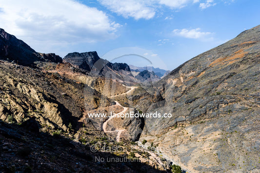 A winding dirt road meanders through a desert mountain pass. Hatt, Wadi Bani Awf, Snake Gorge, Western Hajar Mountains, Ad Dakhiliyah Region, Sultanate of Oman.