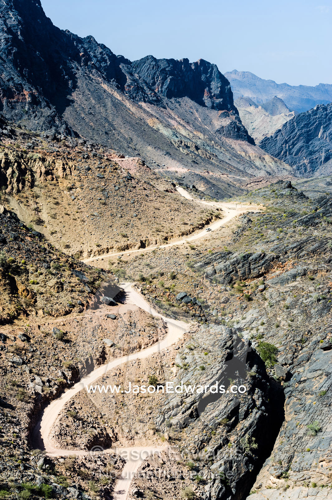 A winding dirt road meanders through a desert mountain pass. Hatt, Wadi Bani Awf, Snake Gorge, Western Hajar Mountains, Ad Dakhiliyah Region, Sultanate of Oman.