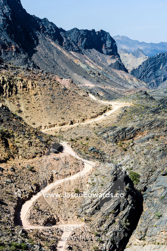 A winding dirt road meanders through a desert mountain pass. Hatt, Wadi Bani Awf, Snake Gorge, Western Hajar Mountains, Ad Dakhiliyah Region, Sultanate of Oman.