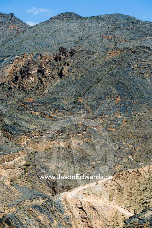A 4WD descends a winding dirt road through a desert mountain pass. Hatt, Wadi Bani Awf, Snake Gorge, Western Hajar Mountains, Ad Dakhiliyah Region, Sultanate of Oman.