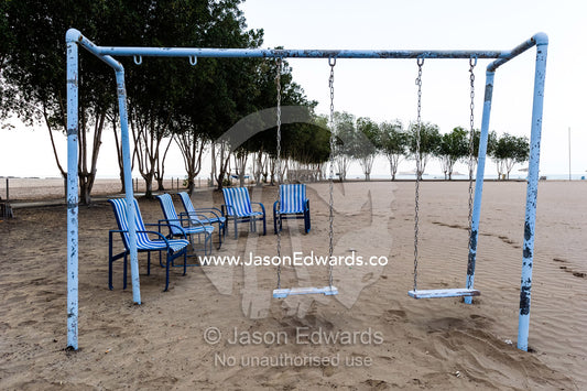 A weathered swing set and deck chairs on an empty beach on the Gulf of Oman. Daymaniyat Islands Nature Reserve, Wilayat AlSeeb, Barka, Sultanate of Oman.