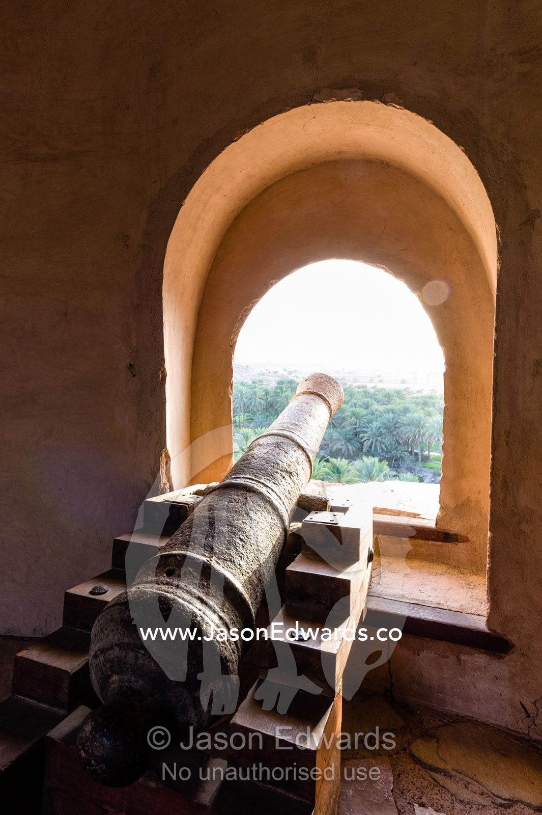 An ancient cannon pointing through a portal defends a fort in the desert. Nakhal Fort, Wilayt Nakhal, Mount Nakhal, Al Batinah South Governorate, Sultanate of Oman.