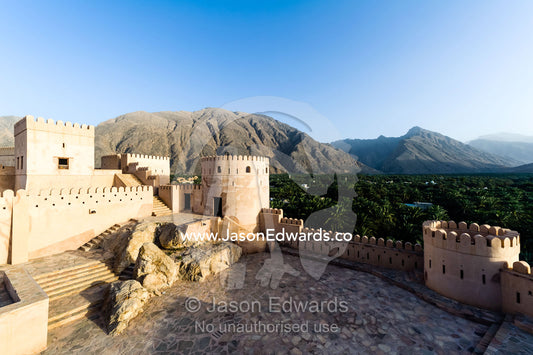 The ancient walls, parapets, battlements and watch tower of a fort on a desert mountaintop. Nakhal Fort, Wilayt Nakhal, Mount Nakhal, Al Batinah South Governorate, Sultanate of Oman.