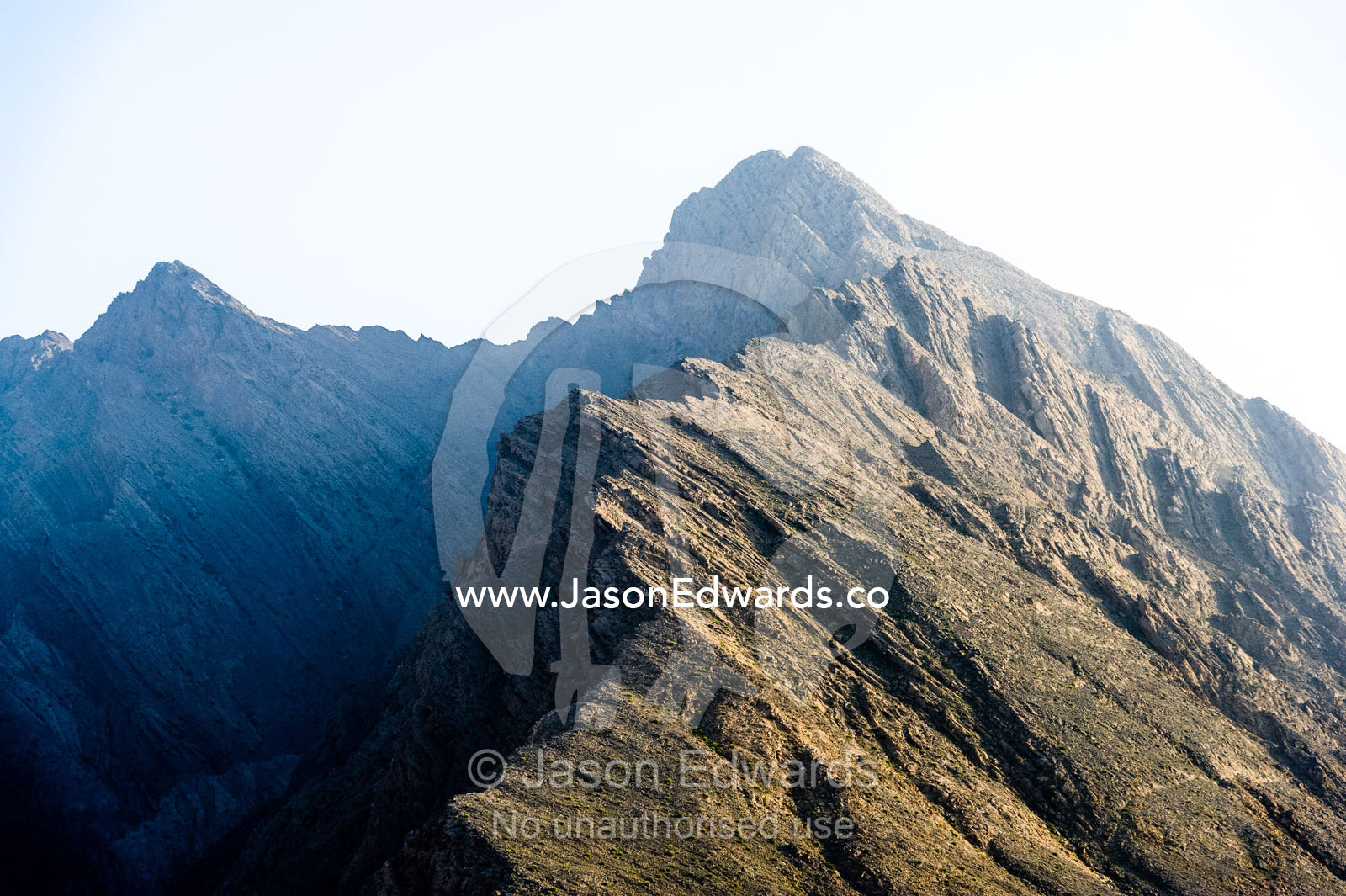 A jagged desert mountain peak catches the last rays of the setting sun. Wilayt Nakhal, Mount Nakhal, Al Batinah South Governorate, Sultanate of Oman.