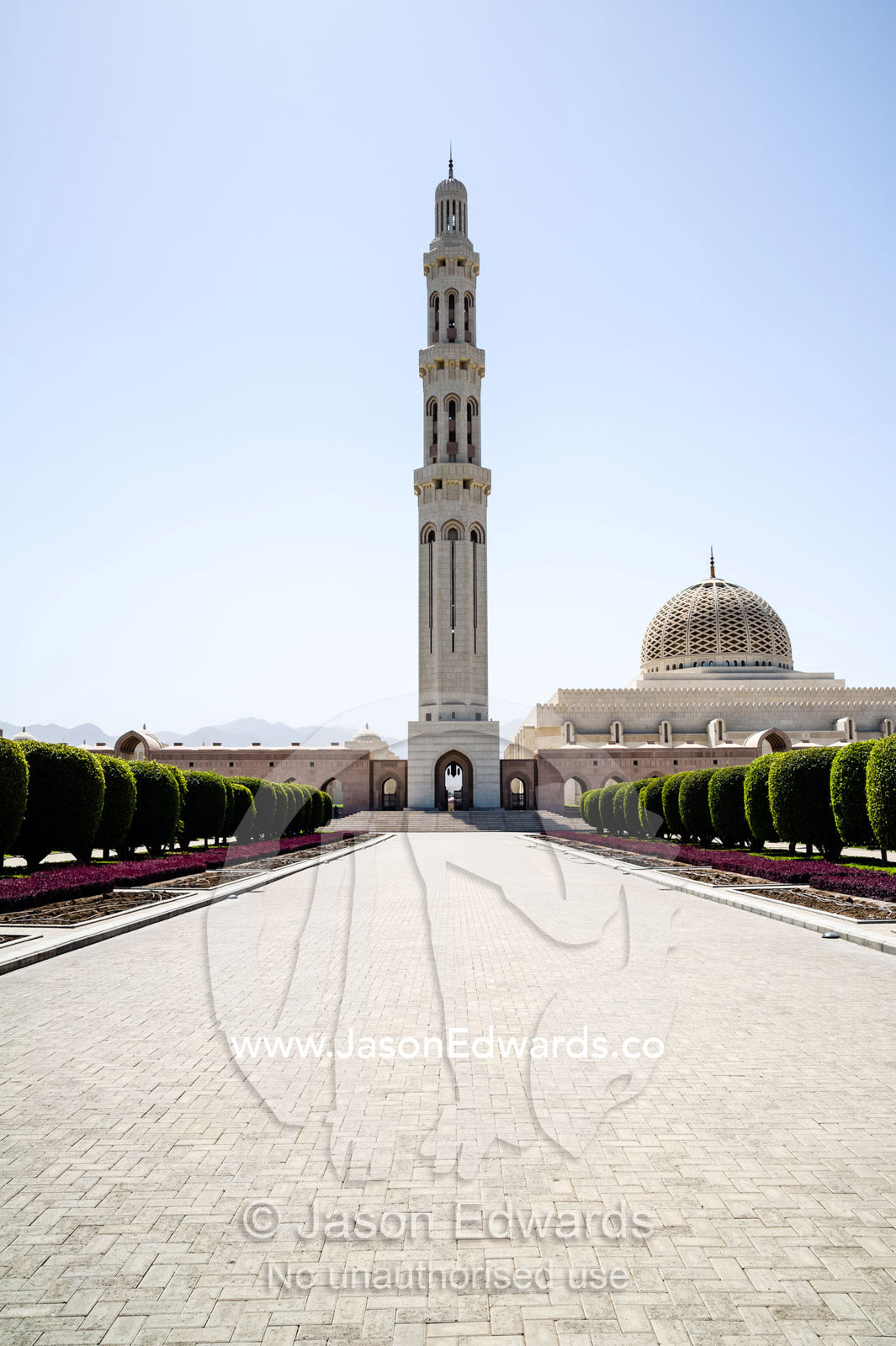 An ornate stone minarette towers over a paved entrance to the Grand Mosque. Sultan Qaboos Grand Mosque, Muscat, Sultanate of Oman.