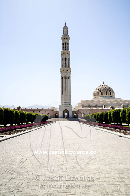 An ornate stone minarette towers over a paved entrance to the Grand Mosque. Sultan Qaboos Grand Mosque, Muscat, Sultanate of Oman.