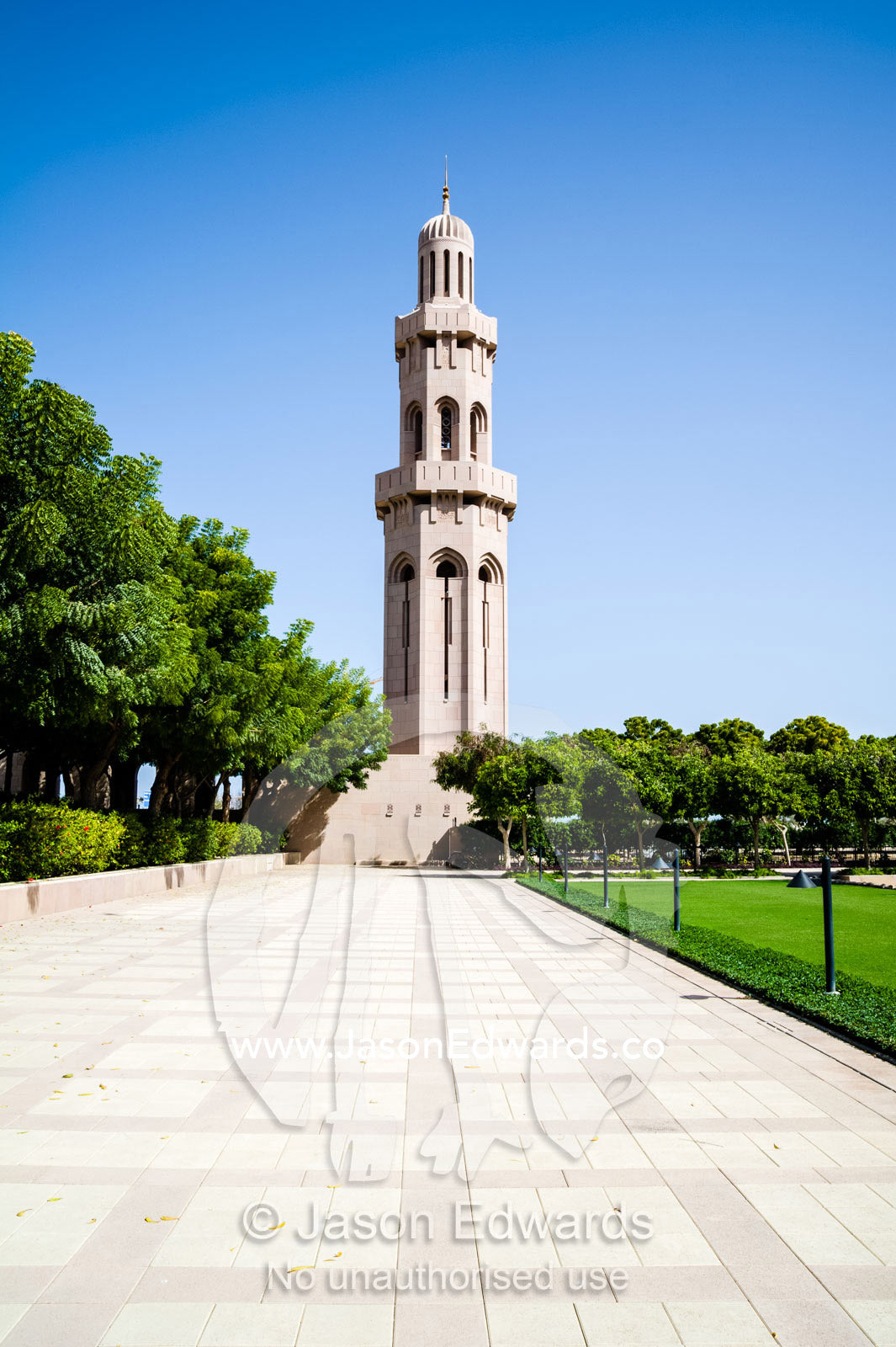 An ornate stone minaret towers over lush gardens in the Grand Mosque. Sultan Qaboos Grand Mosque, Muscat, Sultanate of Oman.