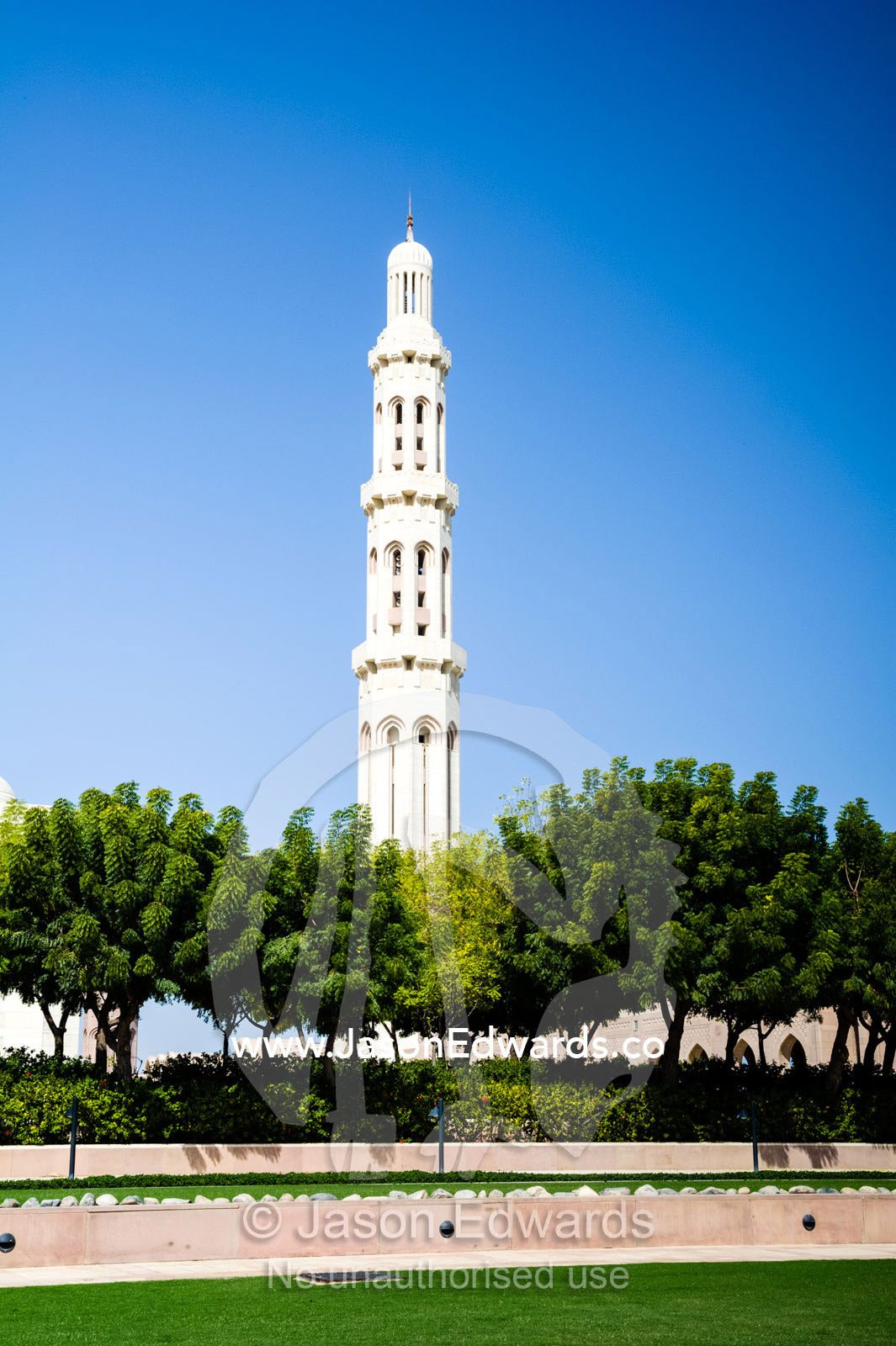 An ornate stone minaret towers over lush gardens in the Grand Mosque. Sultan Qaboos Grand Mosque, Muscat, Sultanate of Oman.